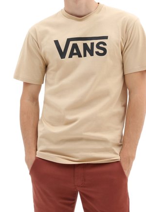 Beżowy bawełniany t-shirt z dużym czarnym logo „VANS” na piersi. Krótkie rękawy i okrągły dekolt, noszony z bordowymi spodniami.
