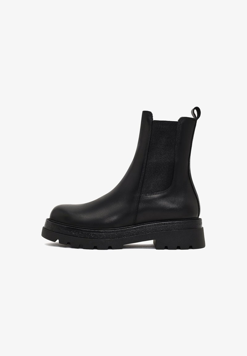 Stivale Chelsea in pelle nera con pannelli elastici laterali, punta rotonda e suola in gomma testurizzata. Presenta una linguetta sul retro.