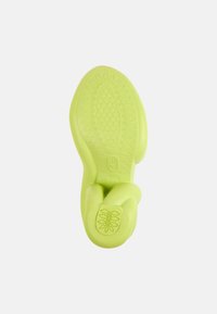 Vihreä kumipohja, jossa on teksturoitu pito ja kaareva muotoilu. Sisältää sileän pinnan ja huomaamattoman logon yksityiskohdan kantapäässä.