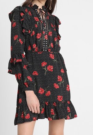 Sort langærmet kjole med røde blomster- og hvide polkaprikmønstre, flæsedetaljer og bindesnøre ved halsen.