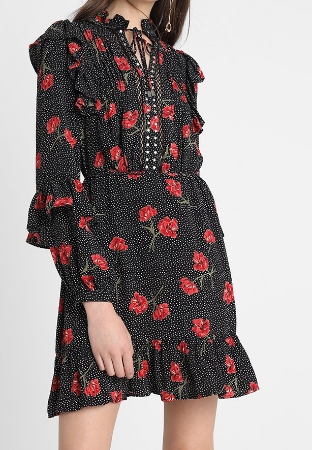Robe noire à manches longues avec motifs floraux rouges et pois blancs, détails à volants et col à nouer.