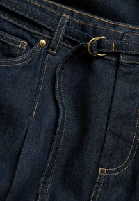 Mörkblå denimjeans med gyllene sömmar, med en metallknappstängning och ett bälteshål. Slät textur med en klassisk design.
