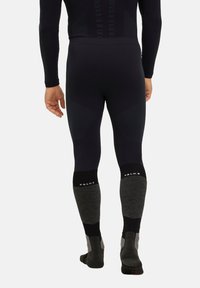 Leggings thermiques noirs avec des sections gris texturé aux genoux et aux chevilles. Présentent une coupe ajustée et un logo contrasté au niveau des poignets de cheville.