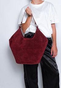 Borsa tote in suede color bordeaux con apertura ampia, manici curvi e texture liscia; presenta un ampio interno per lo stoccaggio.