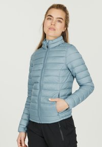 Lys blå pufferjakke med ståkrave, vandret quiltet design, lynlås-lukning og sidelommer, lavet af et glat materiale.