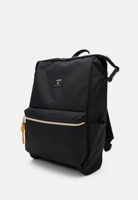 Czarny plecak wykonany z tkaniny o gładkiej fakturze, z złotym zamkiem błyskawicznym, przednią kieszenią oraz metką marki na przodzie.
