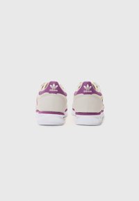 Baskets en suede beige avec des accents violets et des semelles blanches. Présentent un logo sur le talon et un mesh sur les côtés pour la respirabilité.