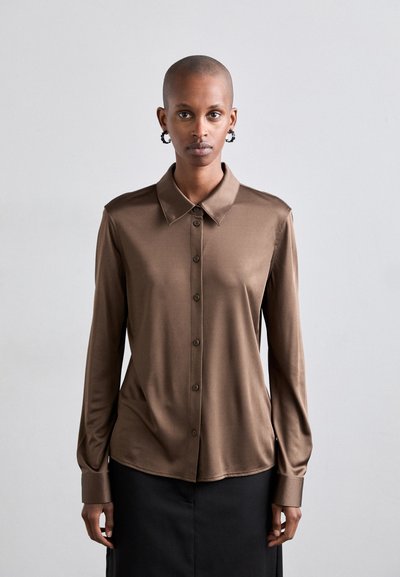 Blouse marron à manches longues en tissu lisse, avec un col, une fermeture à boutons sur le devant et des manches à poignets. Le design est ajusté avec une texture douce.