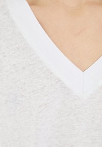 V-neck t-shirt in lightweight, textured white fabric with a contrasting white ribbed neckline. Close-cropped view focusing on collar detail.