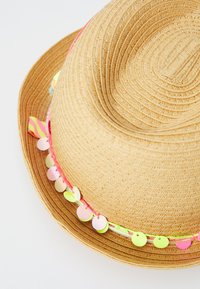 Bézs szalmakalap széles karimával, színes szalaggal, amelyet díszes kerek flitterek díszítenek rózsaszín, sárga és zöld színben a karimán.