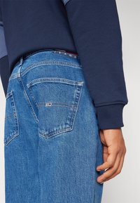 Jeans de denim en un color azul claro con un corte recto, que cuentan con bolsillos estándar y detalles de costura. La cintura tiene una etiqueta.
