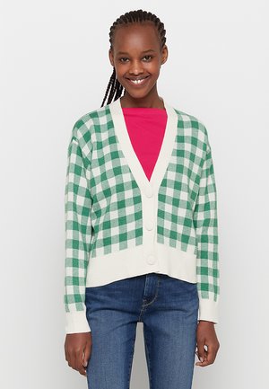 Cardigan a quadri verde e bianco con scollo a V, cinque bottoni e polsini a costine, indossato su una camicia rosa, abbinato a jeans blue.