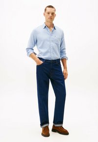 Lysblå skjorte med knapper og en brystlomme, parret med mørkeblå denimjeans og brune ruskindssko. Løs pasform og opsmøget ærmer.