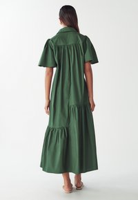 Zelené bavlněné šaty s krátkými nafouknutými rukávy, límečkem, tiered volánkovým lemem a nařaseným designem v zadní části, sahající pod kotníky.