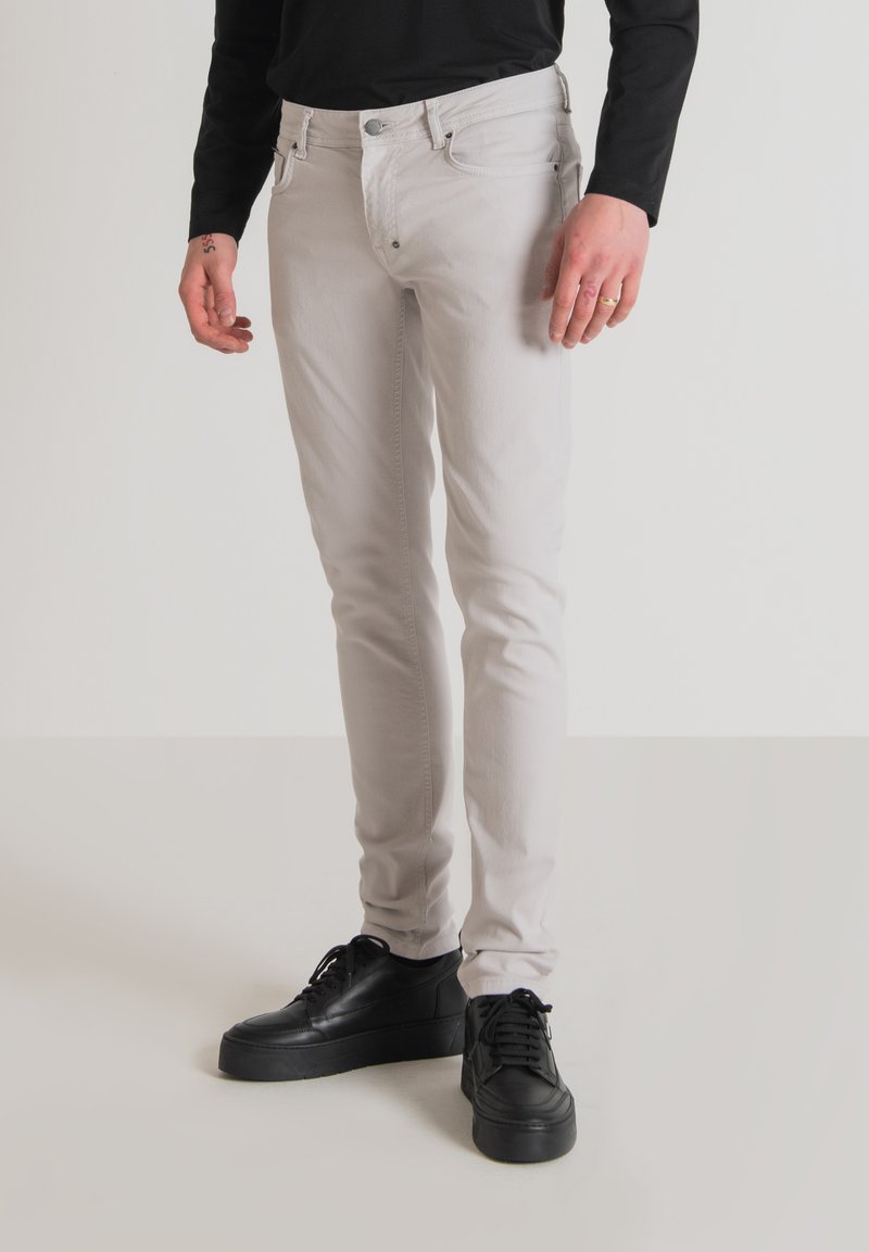 Vaqueros gris claro de denim, con un ajuste slim, diseño de cinco bolsillos y cierre de botón, combinados con zapatillas negras.