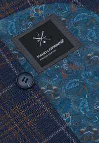 Woven fabric in navy with brown check pattern, featuring a blue floral accent, black label with white branding, and a dark button.