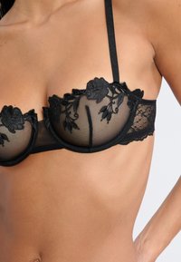 Czarny koronkowy biustonosz z kwiatowym haftem, półprzezroczysta siateczka, wsparcie w postaci fiszbin, regulowane ramiączka oraz falbaniaste wykończenia. Teksturowany i skomplikowany wzór.