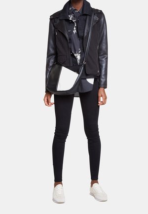 Černá kožená a látková bunda s límcem, černé úzké džíny a bílé tenisky. Taška má černo-bílý design.