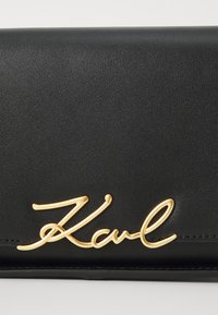Black leather wallet with a smooth texture, featuring a gold "Karl" signature logo as a prominent detail.