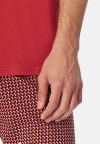 Camiseta roja de manga corta combinada con pantalones ajustados rojos y blancos con estampado. La mano muestra un detallado de la textura de la piel y los dedos.
