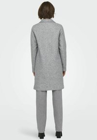 Manteau en laine gris à coupe droite, avec col et manches longues, associé à un pantalon gris clair. Texture lisse, design mi-long et coutures minimales.