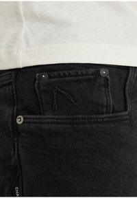 Mustat farkut sisältävät pienen etutaskun, jossa on kolmion muotoinen tikkaus ja kaksi metallista nappia.