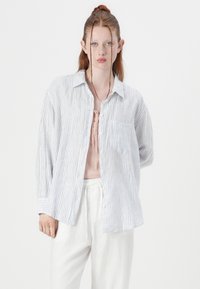 Striped button-up shirt in lightweight cotton fabric, featuring blue and white stripes, long sleeves, a chest pocket, and a relaxed fit.