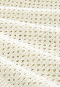 Tessuto bianco lavorato a maglia con un motivo a intreccio aperto e texture, caratterizzato da fori equidistanti che creano un aspetto morbido e traspirante.