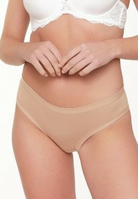Nude naadloze bikini-ondergoed met een gladde textuur, elastische tailleband en minimalistisch design, gecombineerd met een witte kant beha.