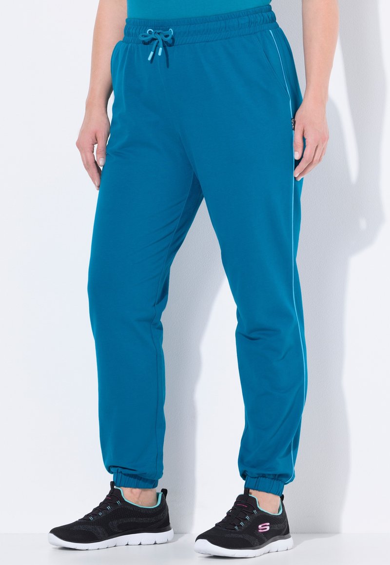 Teal joggers med elastisk midja och justerbar dragsko. Har sidofickor och fåll vid anklarna. Bärs med svarta träningsskor.