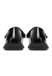 Mocassins en cuir verni noir avec semelles épaisses noires, vus de dos sur fond blanc.