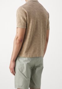 Polo shirt beige a maniche corte in maglia con un motivo a onde texturizzato, abbinato a pantaloni corti verde chiaro, visto da dietro.