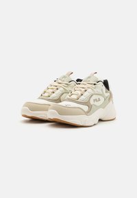 Baskets de sport beige et crème avec une finition texturée, semelle blanche et accents noirs. Elles disposent de lacets et d'un logo sur le côté.