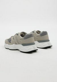 Pareja de zapatillas chunky en beige y gris con suelas gruesas blancas, vistas desde la parte trasera sobre un fondo claro y liso.