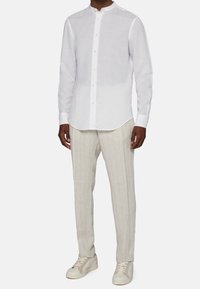 Camicia bianca di lino con bottoni e collo alla coreana, abbinata a pantaloni chiari a righe sottili e sneakers beige. Palette di colori neutri in tutto.