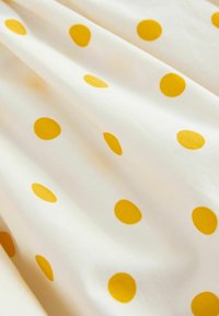 Tela blanca con lunares amarillo brillante uniformemente espaciados y pliegues suaves que crean sombras y textura delicadas.