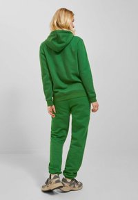 Green sweatshirt and joggers made from soft cotton blend, featuring a hood, ribbed cuffs, and relaxed fit, paired with neutral-colored sneakers.