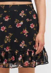 Svart blomsterkjole med rosa og gule blomster. Har en volangkant og en tettsittende midje. Laget av lett, strukturert stoff.