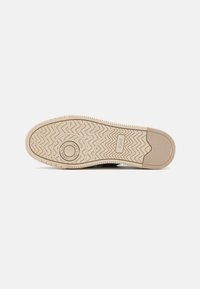 Suola di scarpa in gomma beige chiaro con motivo a zigzag, accentata da un cerchio centrale e con il nome del marchio “TOMS” stampato di lato.