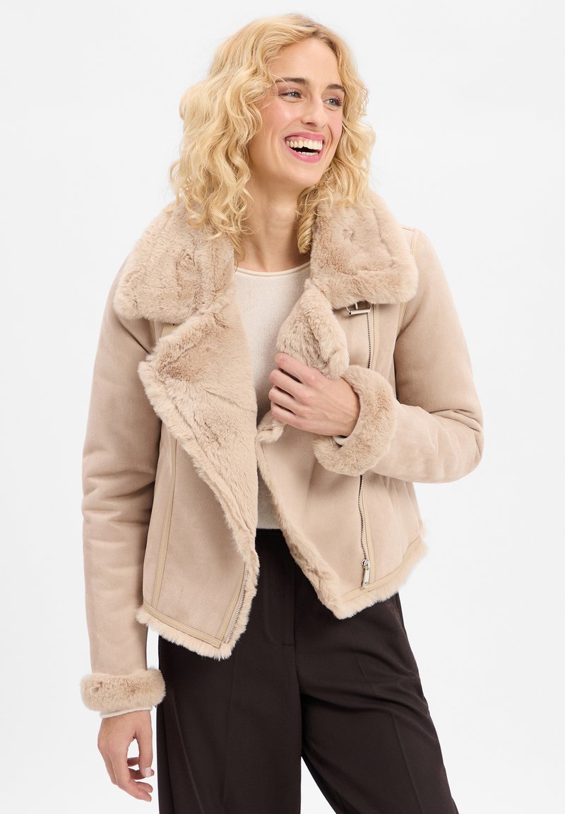Beige Kunstfelljacke mit breitem Kragen, Reißverschluss und flauschigen Manschetten. Glatte Außenseite mit einem weichen, strukturierten Futter.