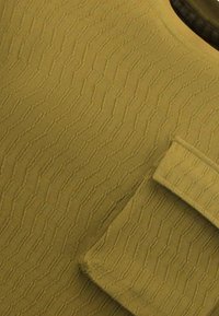 Mosterdgele stoffen textuur met een golfpatroon, met een zak aan de zijkant en een soepele halslijn. Zachte en geweven textuur.