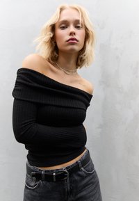 Czarna prążkowana bluzka z opuszczonymi ramionami i długimi rękawami, zestawiona z szarymi dżinsami z wysokim stanem oraz czarnym paskiem z srebrną klamrą.