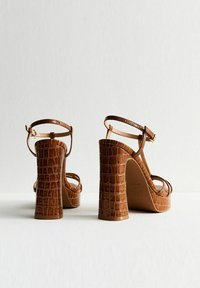 Brown crocodile-embossed high-heeled sandals featuring a platform base, thin ankle straps, and square block heels. Smooth texture and glossy finish.