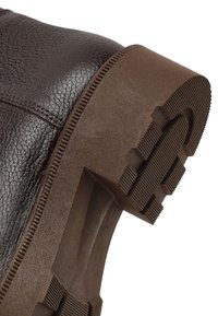 Bruine leren laars met een gestructureerd bovenwerk en een bruine rubberen zool met diepe profielpatronen voor grip. Versterkte naden aan de zijkanten.