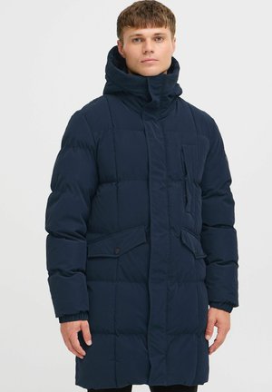 Navy blue puffer coat featuring a high collar, zip and snap closure, front pockets, and ribbed cuffs. Quilted design with a textured finish.