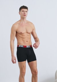 Czarne bokserki z szerokim, czerwono-czarnym paskiem w pasie z logo "DIESEL". Dopasowane, wykonane z gładkiej, rozciągliwej tkaniny.