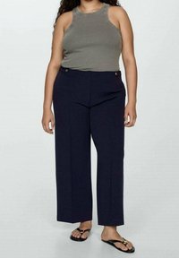 Débardeur gris côtelé, pantalon large bleu marine avec poches avant et accents de boutons dorés, associé à des tongs noires.
