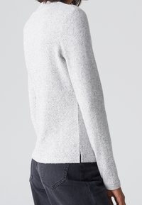 Jasnoszary sweter o fakturowanym wzorze dzianiny. Posiada długie rękawy, okrągły dekolt oraz boczne rozcięcia. W zestawie z ciemnoszarymi spodniami.