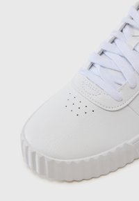 Balti sportiniai bateliai su tekstūruota sintetine viršūne, apvaliu pirštu, perforuotais detalėmis ir iškilniu guminio pado. Visiškai baltos raišteliai.