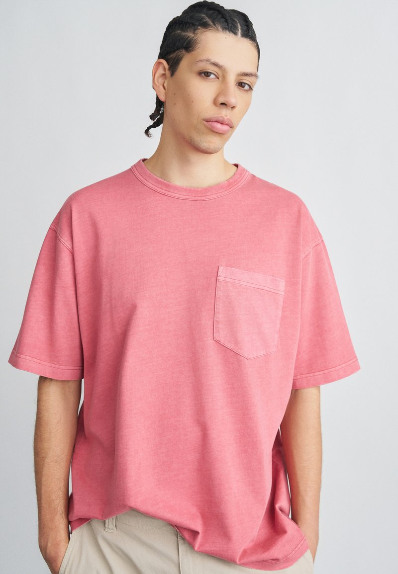 Oversized lyserød t-shirt lavet af blød bomuld, med korte ærmer og en brystlomme. Materialet har en diskret tekstur og en afslappet pasform.